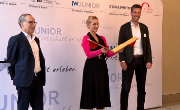 JUNIOR-Startveranstaltung_Startschuss Eine Frau steht in der Mitte von zwei Männern und klappt eine Startklappe zusammen.