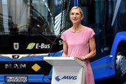 Eine Frau steht an einem Pult vor einem Bus und hält eine Rede. 