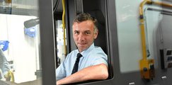 Ein Mann sitzt am Steuer eines Busses und lehnt sich aus dem Fahrerfenster.